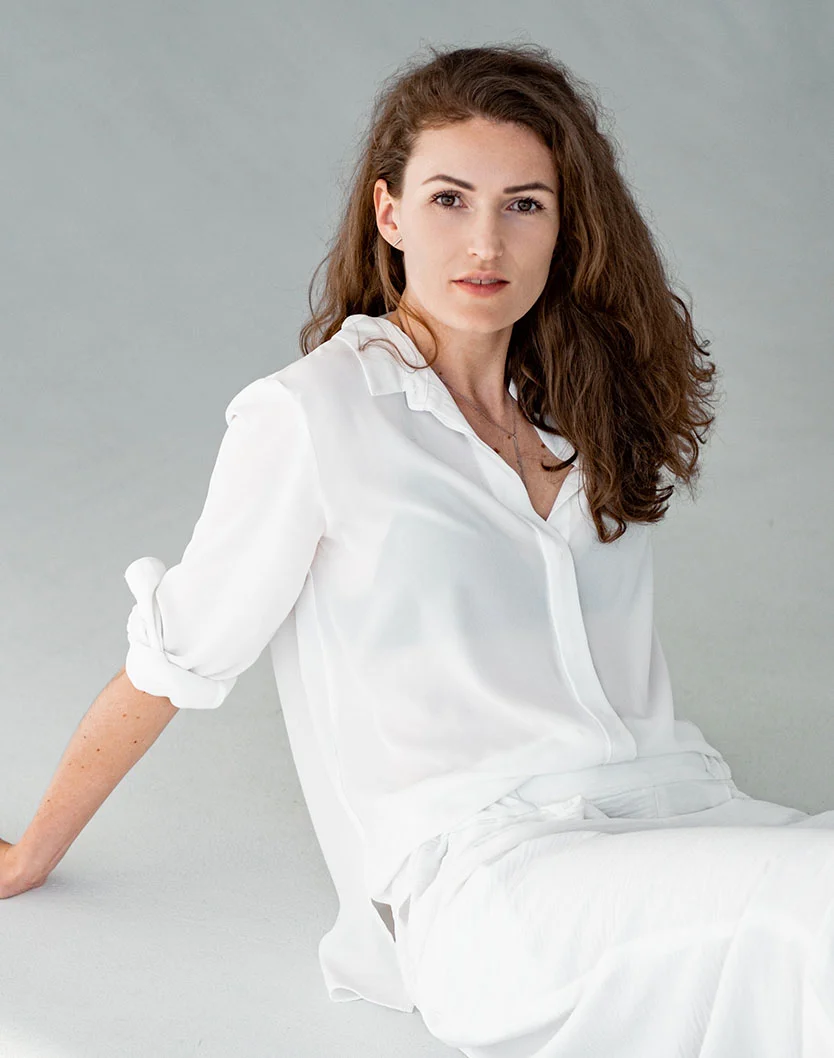 A young woman with curly hair sits gracefully against a soft, neutral background, wearing a white blouse and relaxed expression. - Facetite in West Chester Pike Newton Square, PA